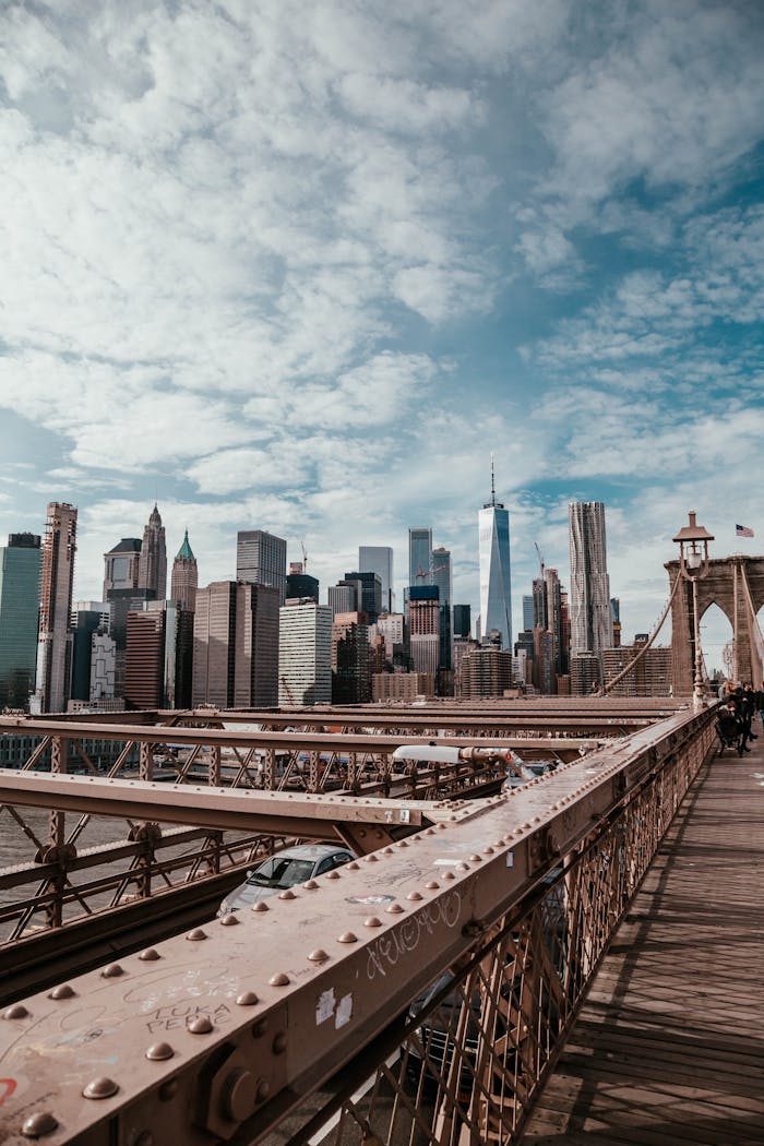 A breathtaking view of the New York City skyline from the Brooklyn Bridge, featuring iconic skyscrapers under a cloudy sky.